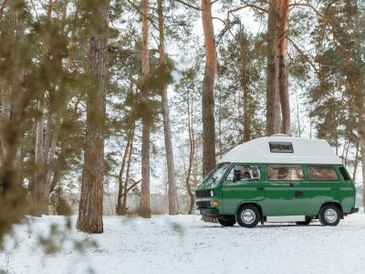 Explore the tranquil beauty of winter with a classic green camper van parked in a snowy forest.